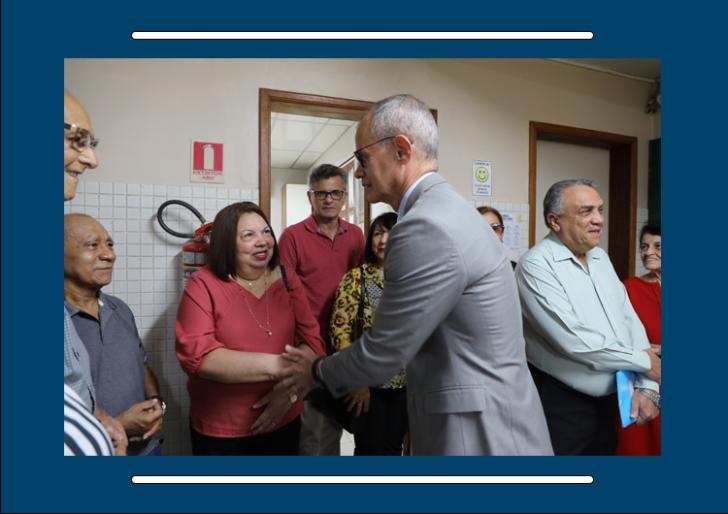 Descrição de imagem: Fotografia em ambiente fechado, nela, está o presidente do tribunal cumprimentando umas das aposentadas. 