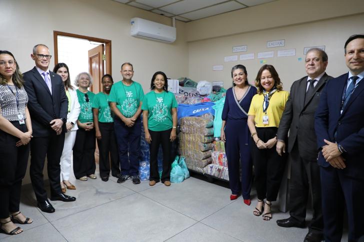 Foto colorida do momento da entrega de alimentos. Próximo às doações, sete representantes do TRT8, incluindo o presidente, e quatro representantes da Comundiade Mar a Dentro posam para foto. 