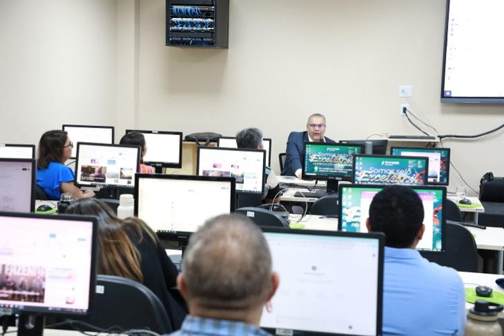 Fotografia colorida da sala de informática da Dinfa, contendo servidores e servidoras prestando atenção no desembargador  do Trabalho Carlos Zahlouth Júnior.