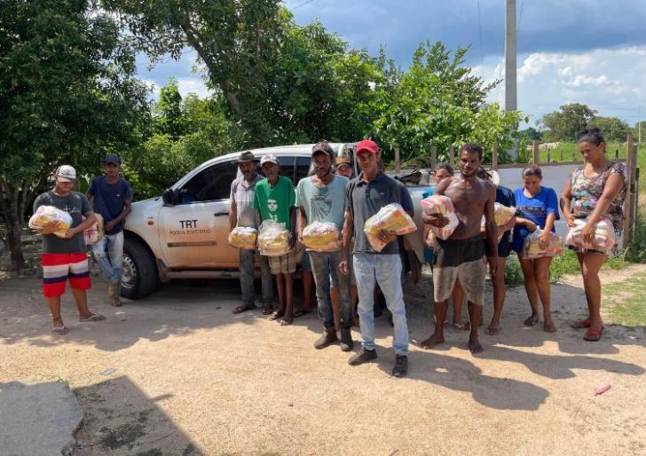 Fotografia com onze pessoas de pé segurando cestas básicas. 