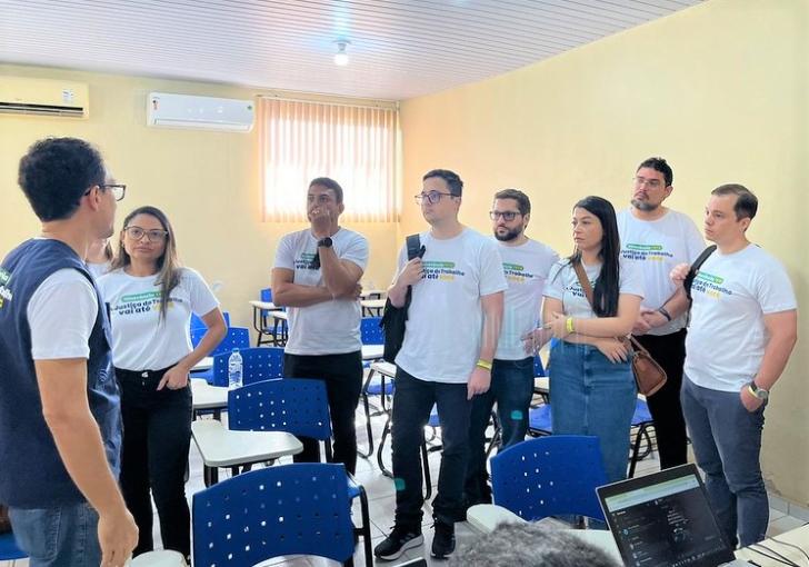 Foto colorida. O juíz Avertano Klautau, diante de outros magistrados, dá orientações sobre a itinerância. No ambiente de sala de aula, todos estão de pé e usam camisa branca da itinerância do trt8.