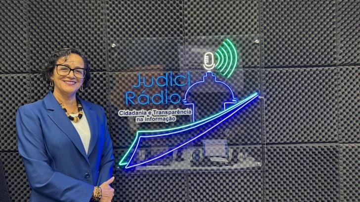 Foto colorida da juíza Núbia Guedes posando ao lado da logo da rádio do TJ Amapá.