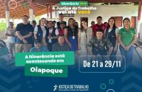 Fotografia colorida com várias pessoas reunidas. No topo, o slogan: Itinerância TRT8. A Justiça do Trabalho vai até você. Abaixo, o texto: A itinerância está acontecendo em Oiapoque. De 21 a 29 de novembro.