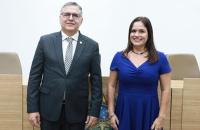 #ParaTodosVerem: Fotografia em ambiente fechado que reúne lado a lado, um homem branco de terno escuro e uma mulher branca de vestido azul