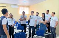 Foto colorida. O juíz Avertano Klautau, diante de outros magistrados, dá orientações sobre a itinerância. No ambiente de sala de aula, todos estão de pé e usam camisa branca da itinerância do trt8.