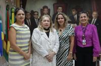 Descrição de imagem: Fotografia em ambiente fechado, nela, estão quatro mulheres de pé e sorrindo para a foto.