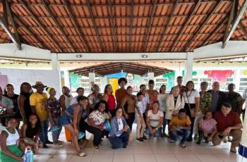 Foto colorida de um grande grupo de moradores de curiaú junto a magistrados do TRT8 em visita a uma escola local